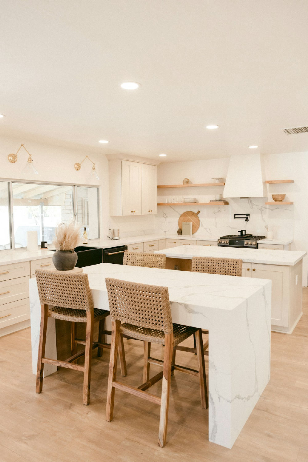 A warm, softly lit kitchen with a marble island and woven stools